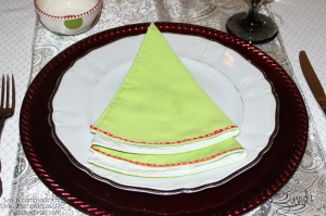 Linen napkin, green lined with white, then trimmed with red ribbon/white polka dots. Folded to the shape of Christmas tree.
